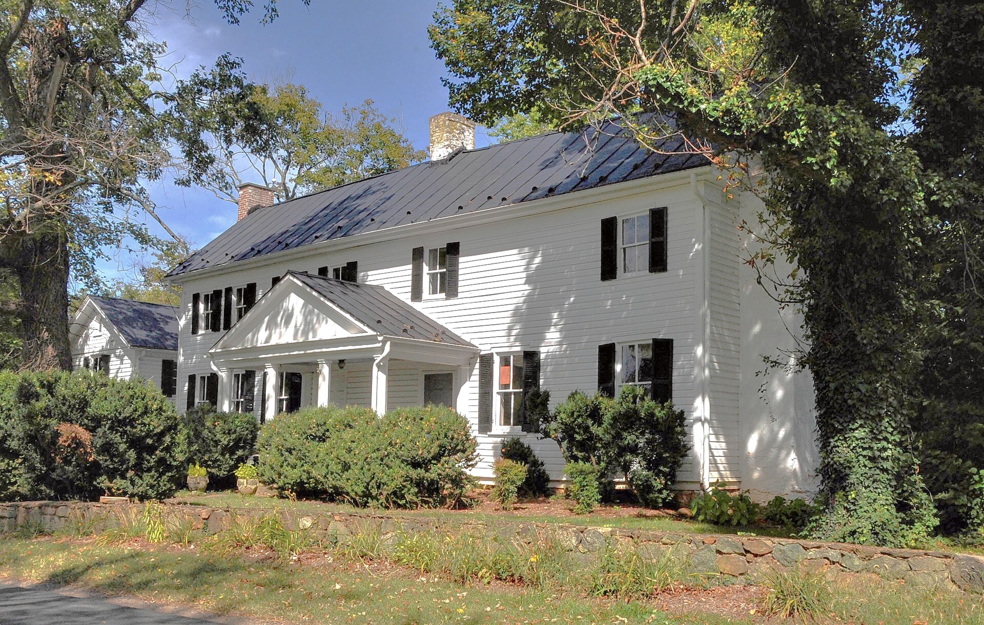 A white Federal farmhouse behind a stone wall in Loudoun County